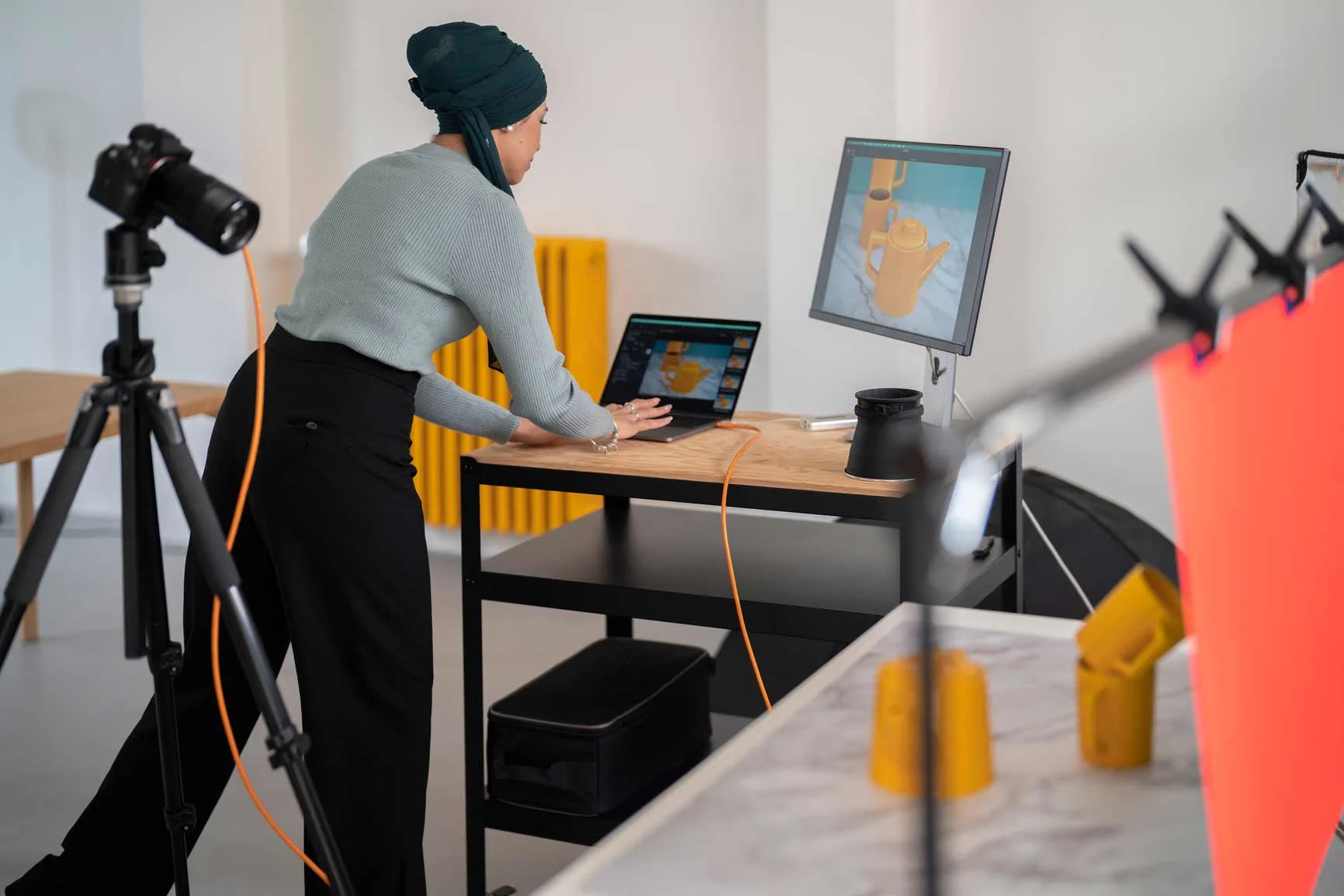 Persoon bewerkt een 3D-model van een hand op een laptop en monitor in een fotostudio met camera en verlichting.