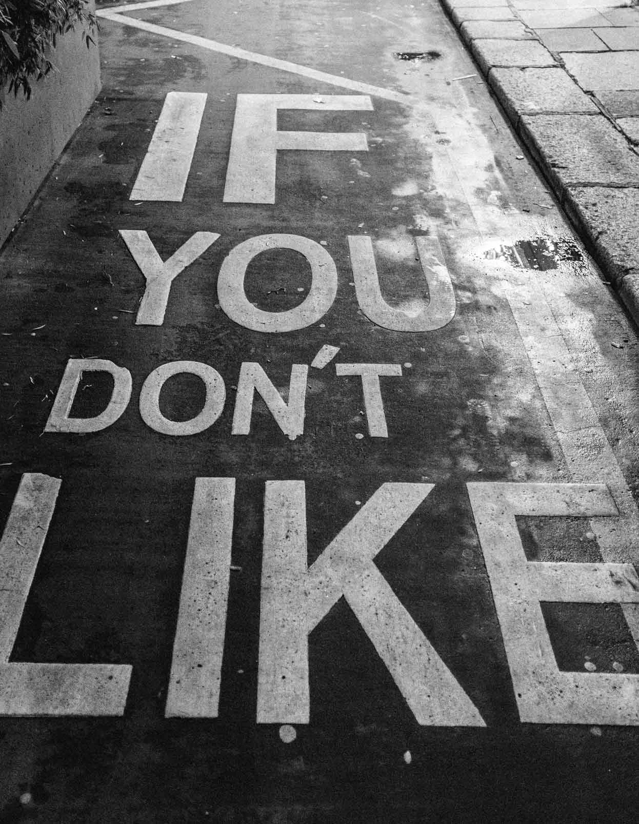 White words “IF YOU DON'T LIKE” are written in capital letters on the asphalt of a sidewalk.