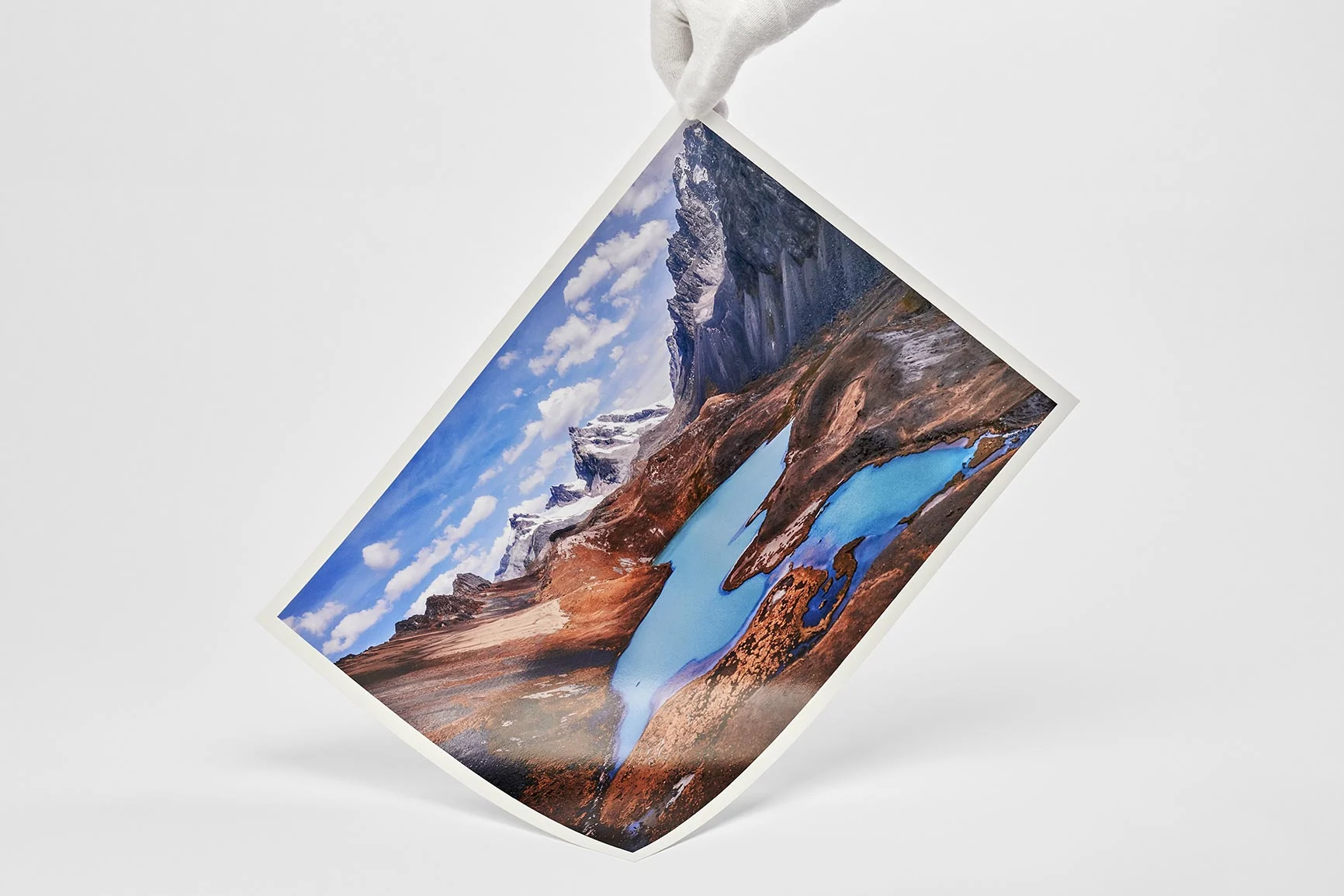 Hand mit weißem Handschuh hält einen Fotodruck mit Landschaftsmotiv auf glänzendem Fine Art Papier.