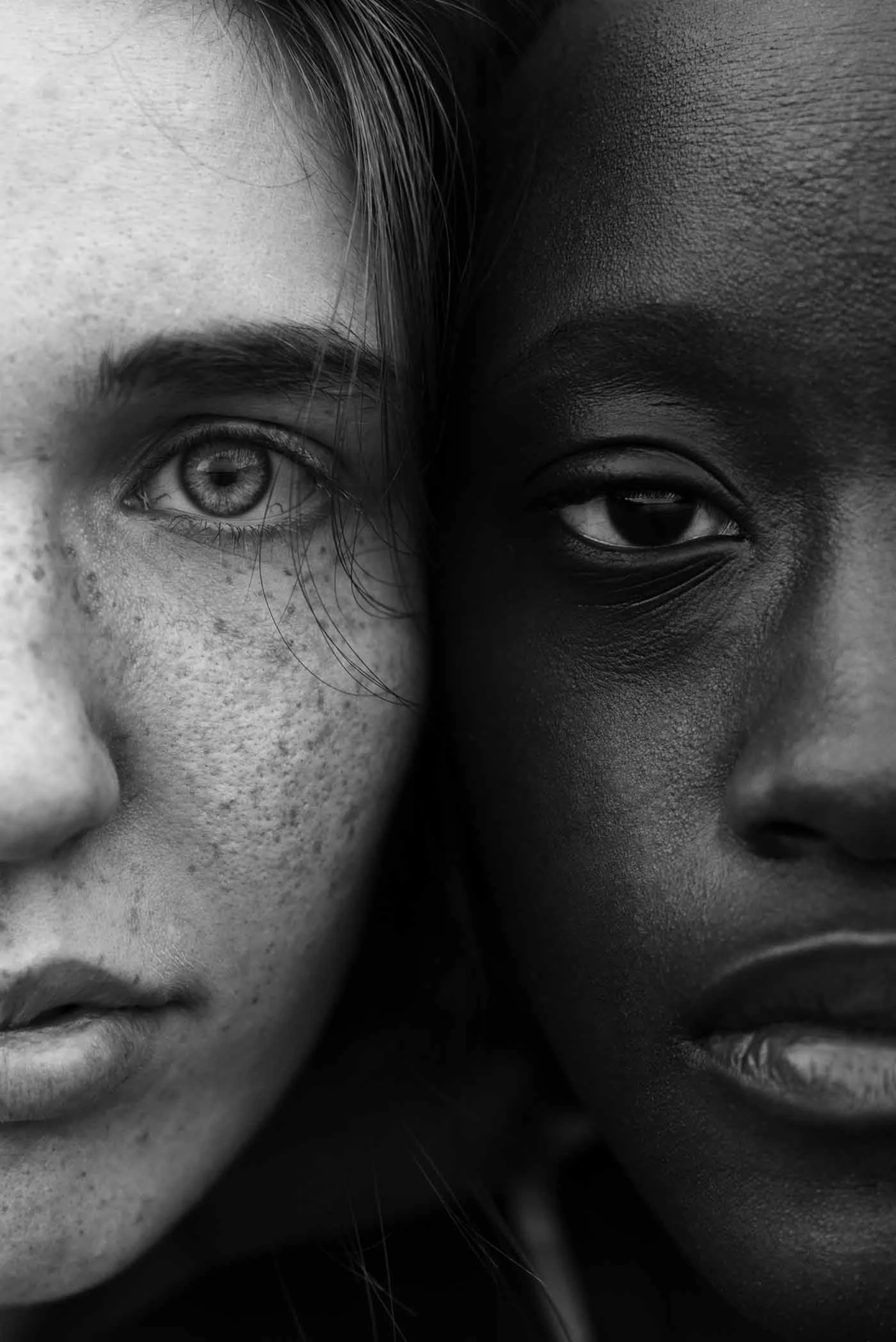 Close-up of two faces next to each other. Both people are looking directly into the camera, the person on the left has freckles.