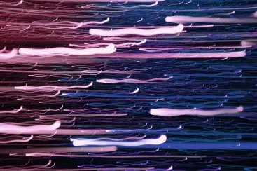 Long exposure with horizontal light trails in pink, violet and blue on a dark background.