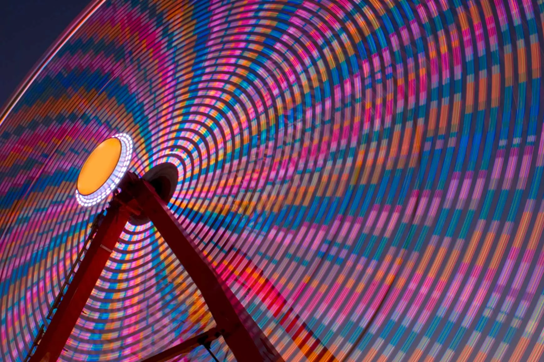 Noria gigante girando con luces de colores en un patrón de círculos concéntricos por la noche.