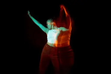 Mujer con top blanco sin mangas bailando sobre un fondo negro, el movimiento crea un efecto de doble exposición.