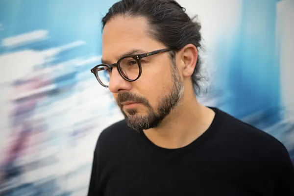 Portrait of a middle-aged white man photographed in profile, wearing black glasses and sporting long black hair.