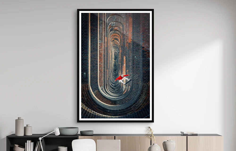 Skater doing an ollie in a viaduct as a photo in a gallery frame hanging on a wall.
