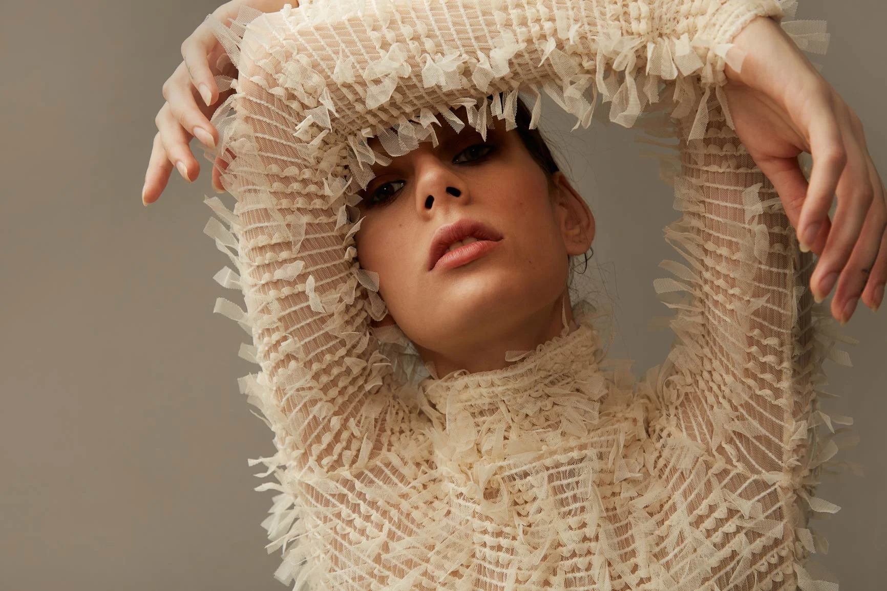 A woman with her arms raised is wearing a sheer, textured top with ruffles and fringe.