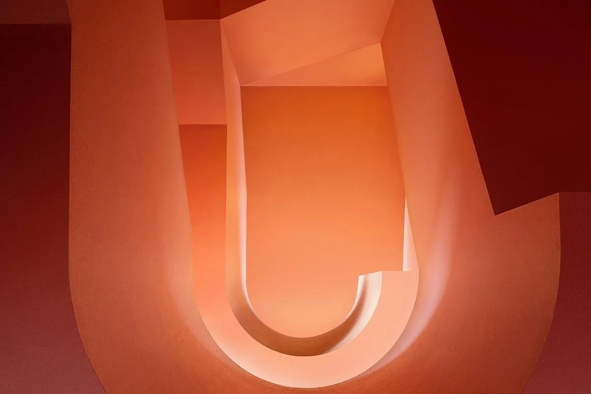 Abstract architecture with curved orange walls and light streaming through openings.