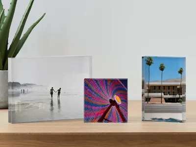 Tre blocchi fotografici in acrilico su una mensola in legno che mostrano una coppia in spiaggia, una ruota panoramica colorata e una scena con palme.