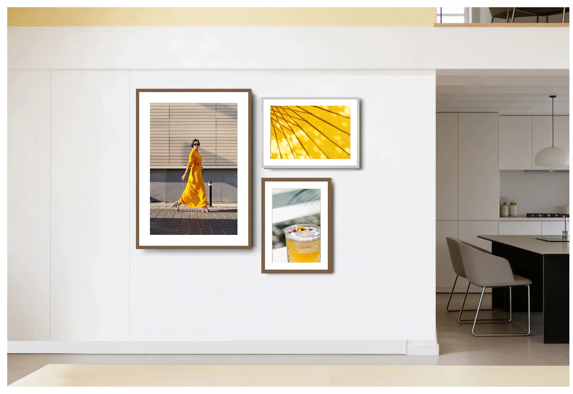Una disposizione asimmetrica di tre immagini incorniciate su una parete bianca in un'area soggiorno e cucina moderna. A sinistra, un grande ritratto verticale di una donna in giallo; alla sua destra, due foto più piccole sovrapposte verticalmente: in alto, un motivo a linee gialle astratto, in basso, un cocktail giallo. Le cornici sono in look legno marrone e argento.