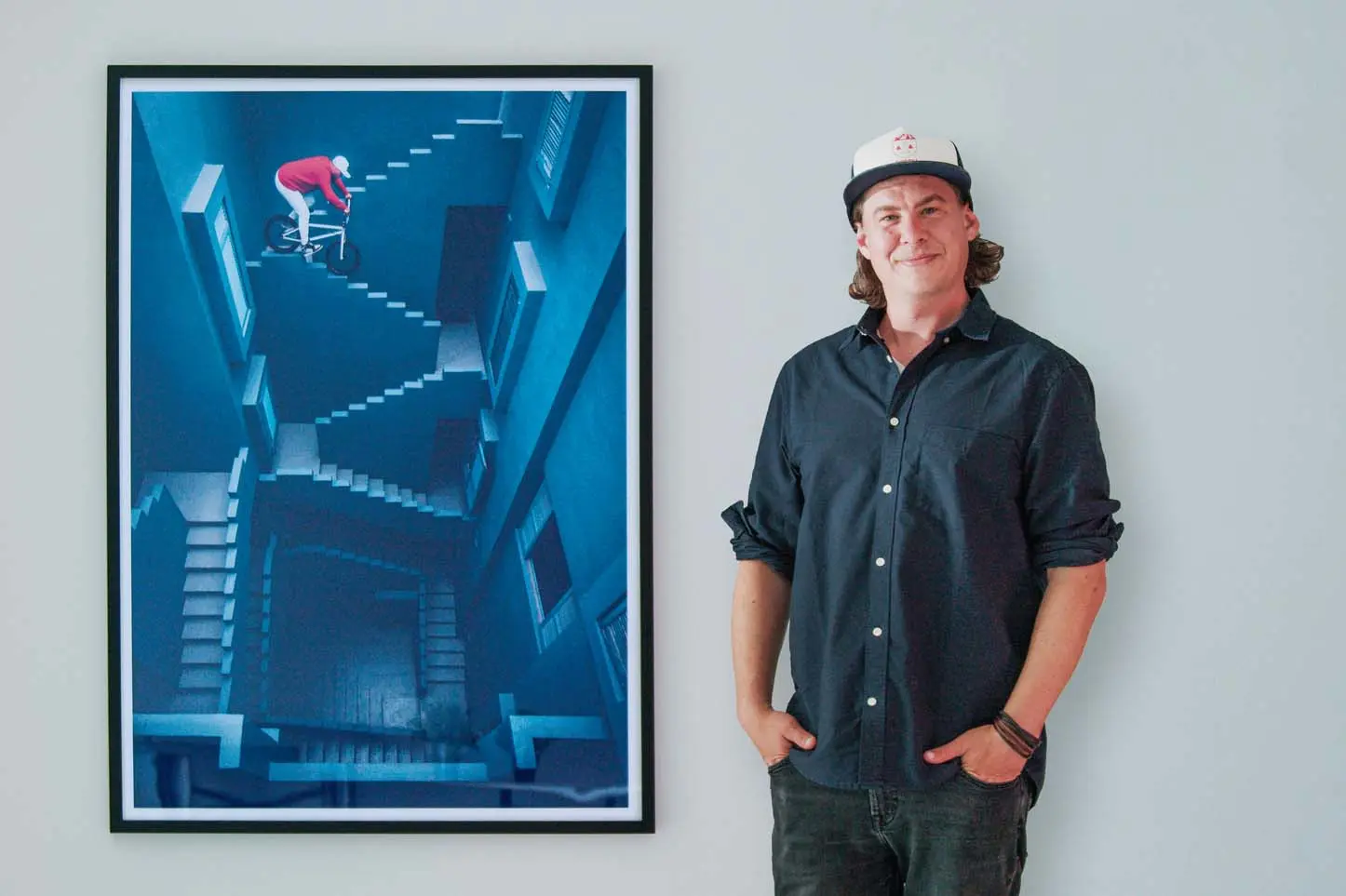 Lorenz Holder standing next to his photo of a BMX athlete riding down stairs as an acrylic photo print in a solid wood gallery frame.