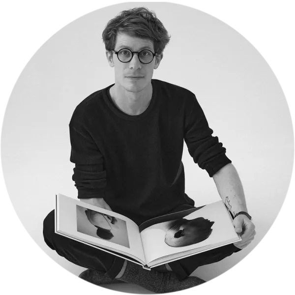 Portrait of Alexandre Souêtre, sitting on the ground with an open Coffee Table Book.