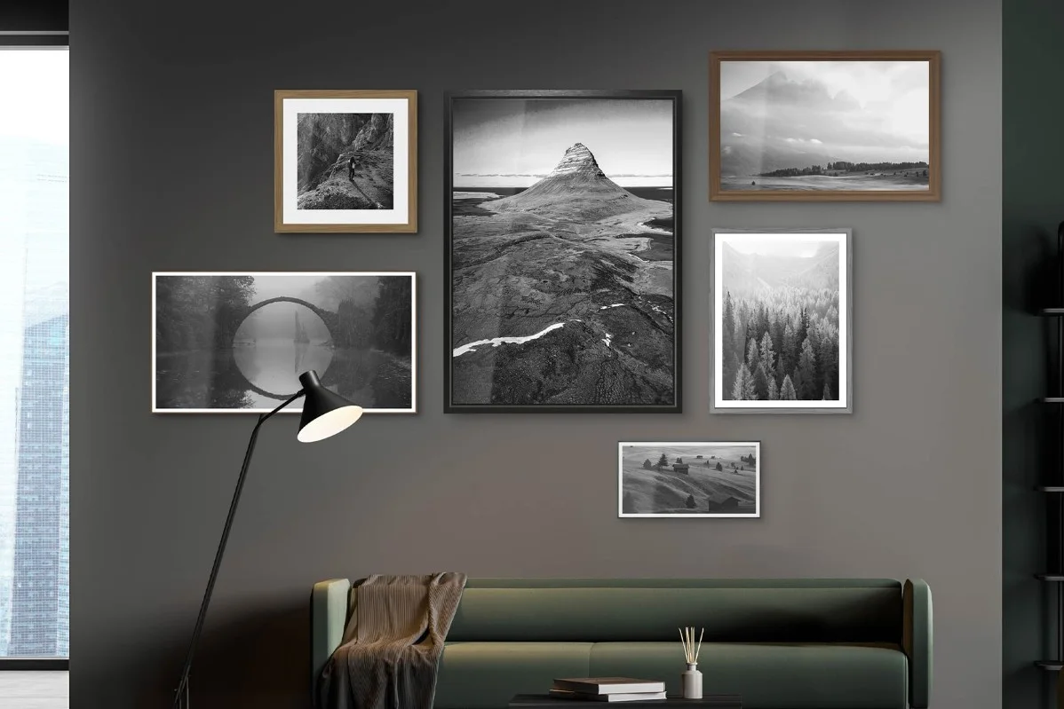 Soggiorno con parete grigio scuro, divano verde, lampada da terra e sei fotografie di paesaggi in bianco e nero con cornici diverse.