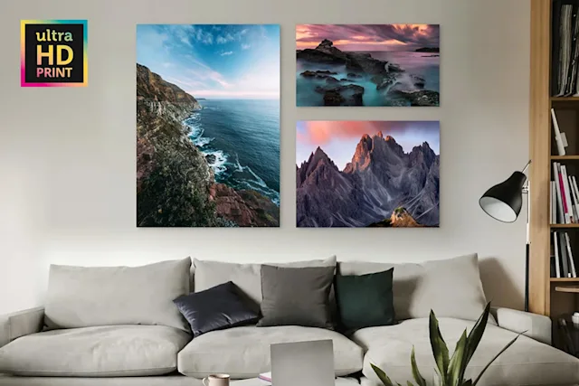 Drei Landschaftsfotografien mit Küste, Felsen und Bergen hängen über einem grauen Sofa mit mehreren Kissen in einem Wohnzimmer.