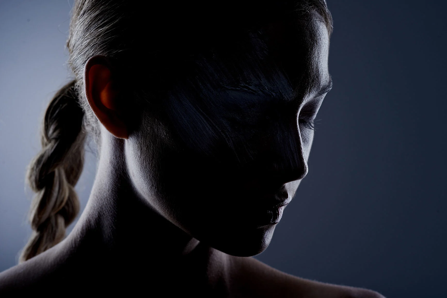 Portrait of a woman with her hair braided to the side, against a dark background with side lighting.