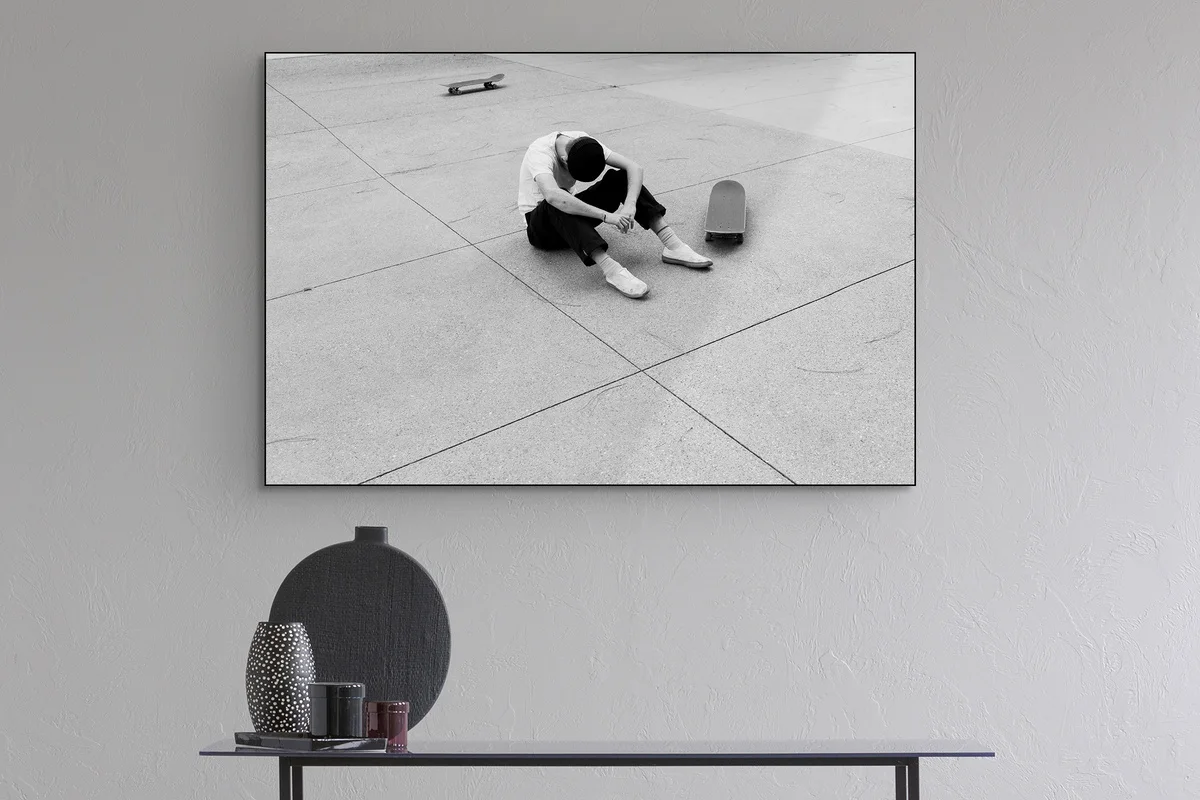 Black and white photo of a skater sitting next to his skateboard.