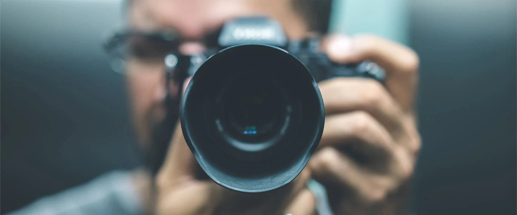 Portrait von einem Mann mit einer Kamera mit großem Objektiv vor dem Gesicht.