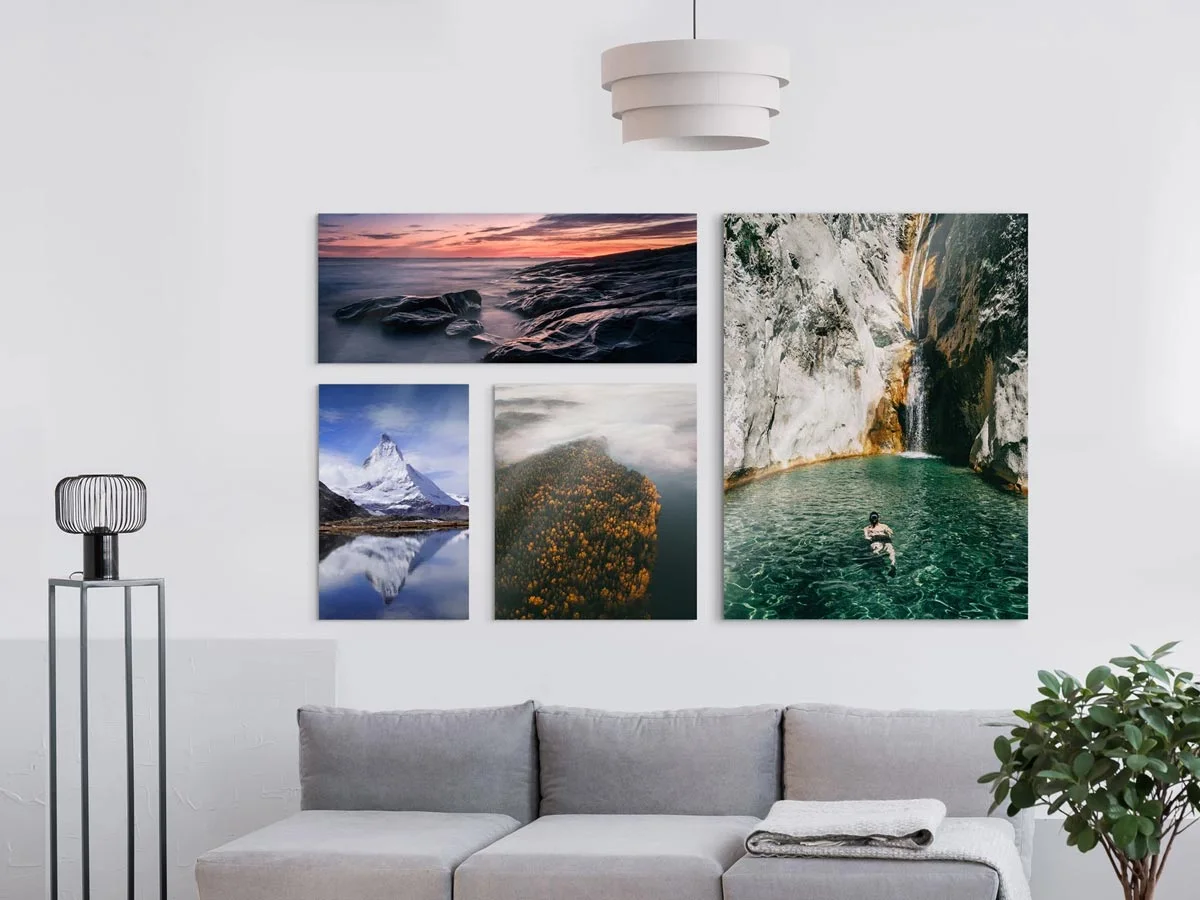 Acrylic glass pictures, hung in a grid pattern on a wall above a sofa: The motifs show a sunset by the sea, a reflection of the Matterhorn, a misty forest and a waterfall with a person in the pool.