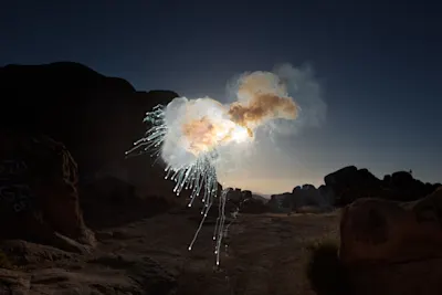 Firework explosion with smoke and sparks in a dark rocky landscape.