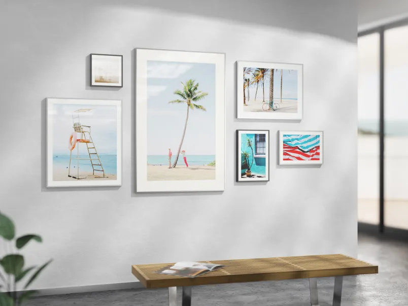 Wall with several magnet framed prints. The prints show different scenes at a beach with palm trees and towels and a high seat for a lifeguard.