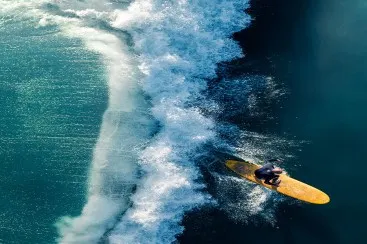 Surfer on yellow board riding a large wave breaking in the blue sea, aerial view.