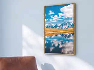 A wood-framed mountain landscape print hangs above a brown leather chair, with a close-up detail of the frame on the right.