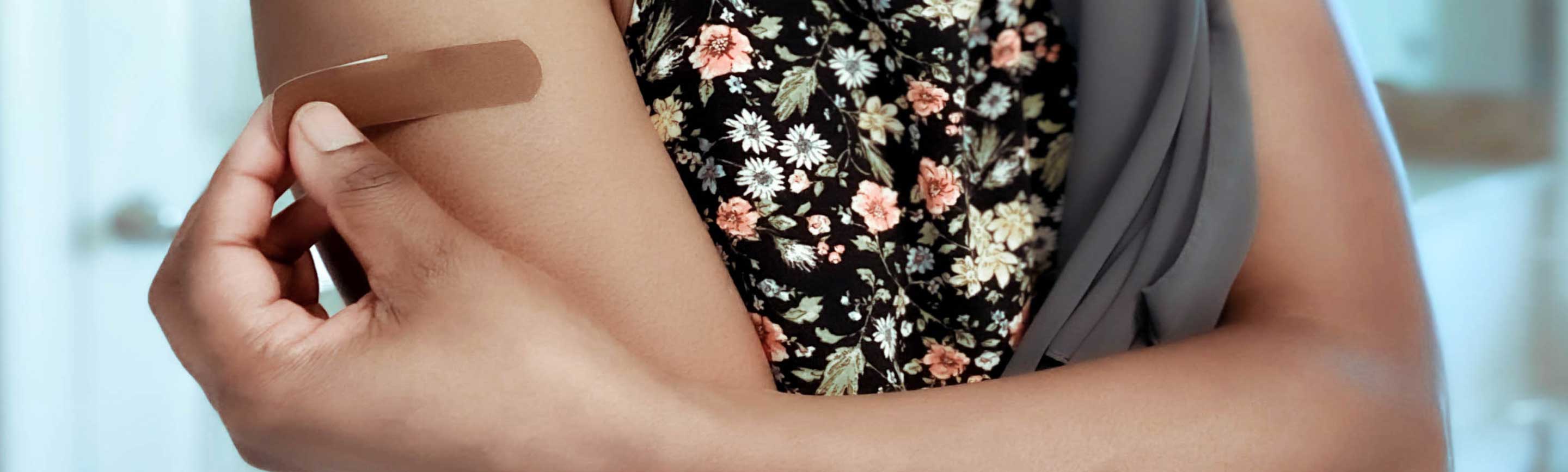 Close-up of a person wearing a floral dress with a bandage on their upper arm, illustrating a minor wound.