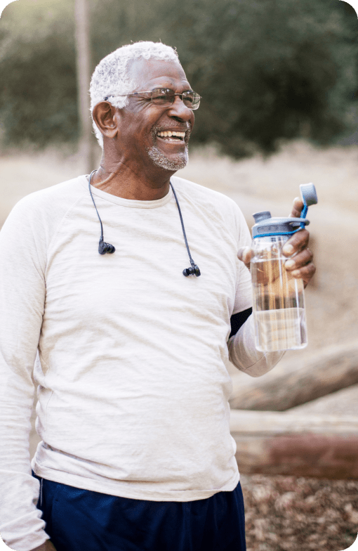 Man smiling and holding a water while taking a walk outdoors.