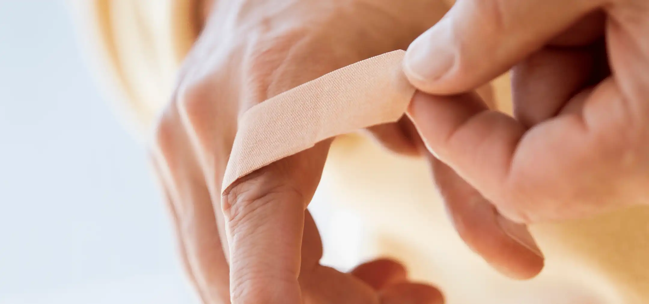 Close-up of a person applying a bandage on their finger, focusing on the hand and the bandage.