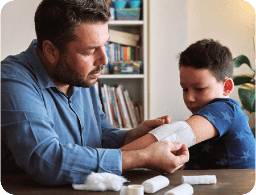 Man placing a bandage over a small boy’s wounded elbow.