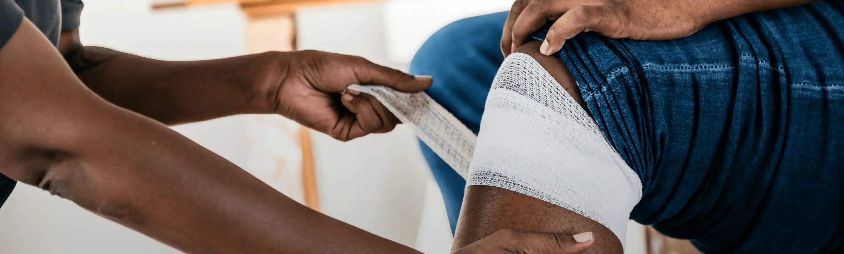 Person using BAND-AID® Brand Gauze to wrap a wound on a knee.