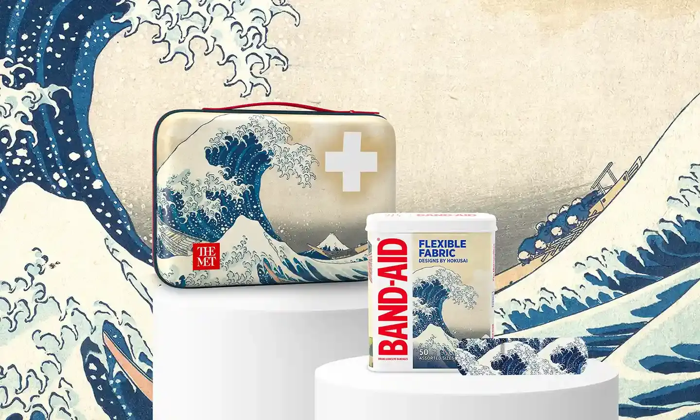 BAND-AID®️ Brand products featuring The Great Wave off Kanagawa design, including a case with a white cross symbol and a container of flexible fabric bandages, part of THE MET collaboration.