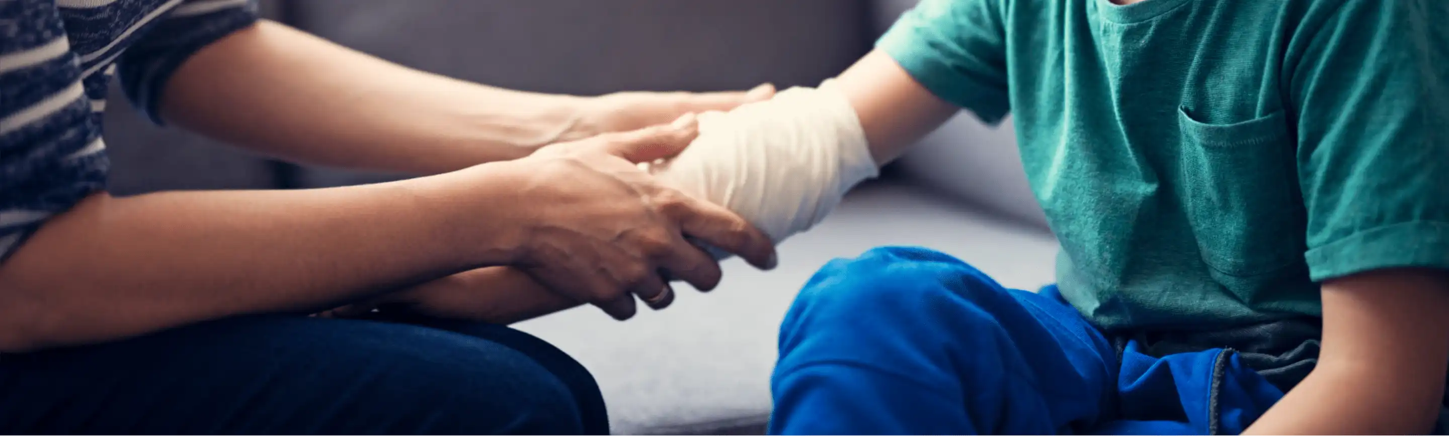 A person carefully inspects and tends to a child's bandaged arm, emphasizing the importance of follow-up care after an injury.