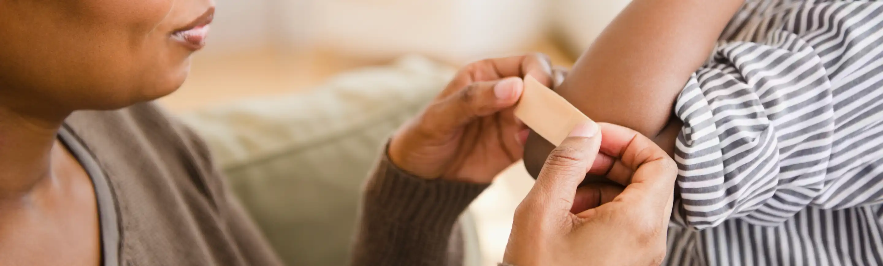 A person applying a Band-Aid bandage to a child's arm, illustrating the use of first aid kit essentials for minor injuries.