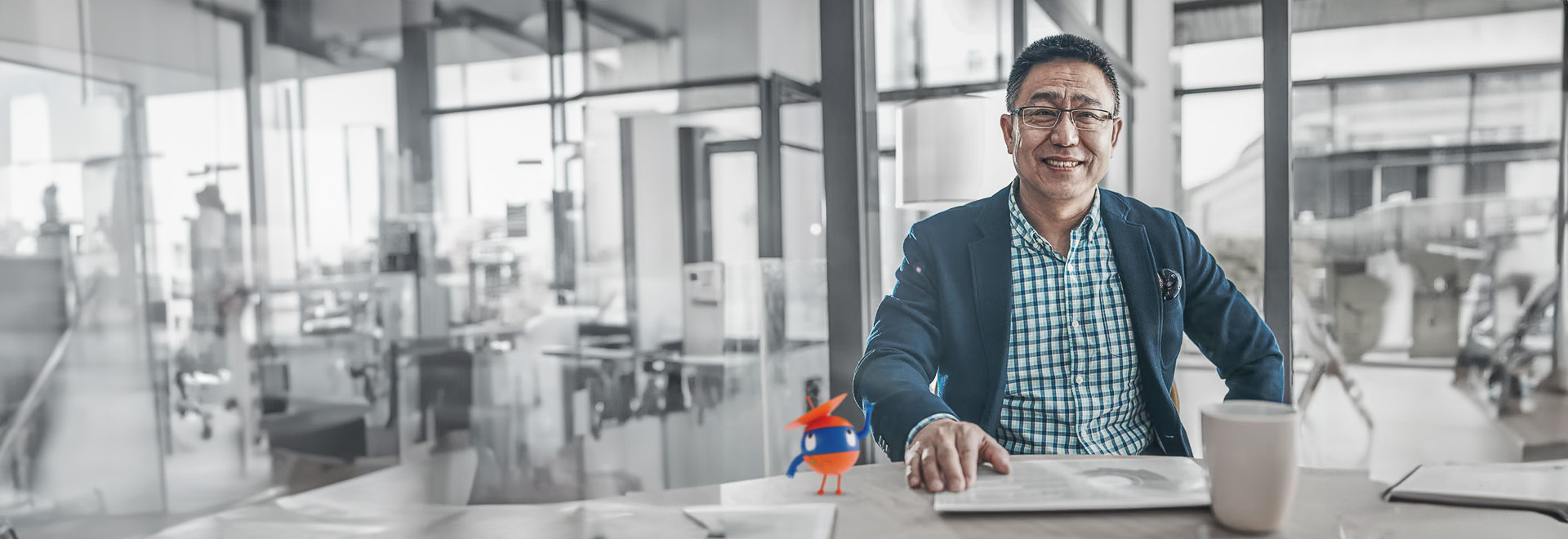 smiling man sitting at a table with a laptop and a cup