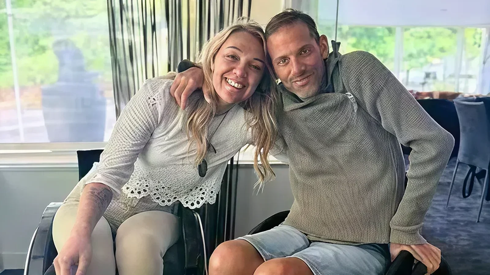 Two wheelchair users smiling together in a bright indoor room.