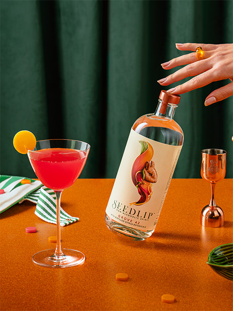 A bottle of seedlip Grove 42 on a bench with slices of orange next to it