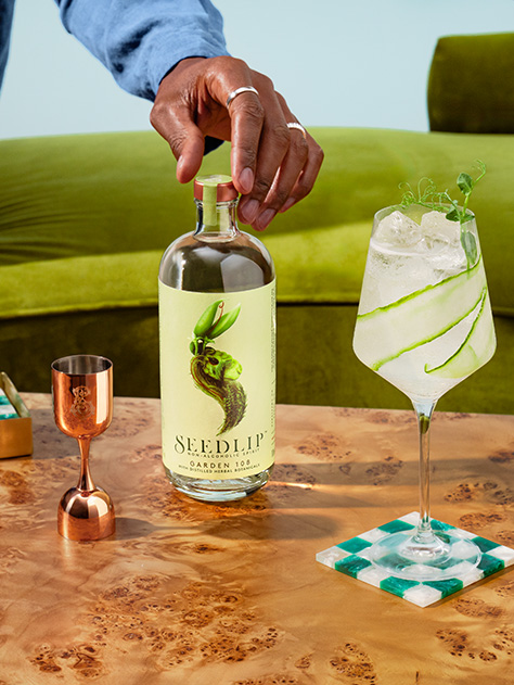 une bouteille de Seedlip Garden 108 sur une surface verte entourée des ingrédients utilisés pour la fabrication de la boisson