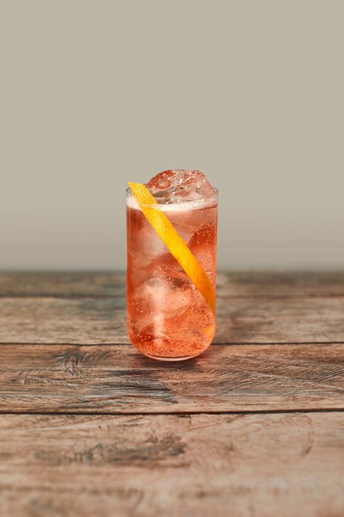 Panoma Seedlip Spice 94 cocktail in a tall glass with ice cubes, garnished with a long orange peel