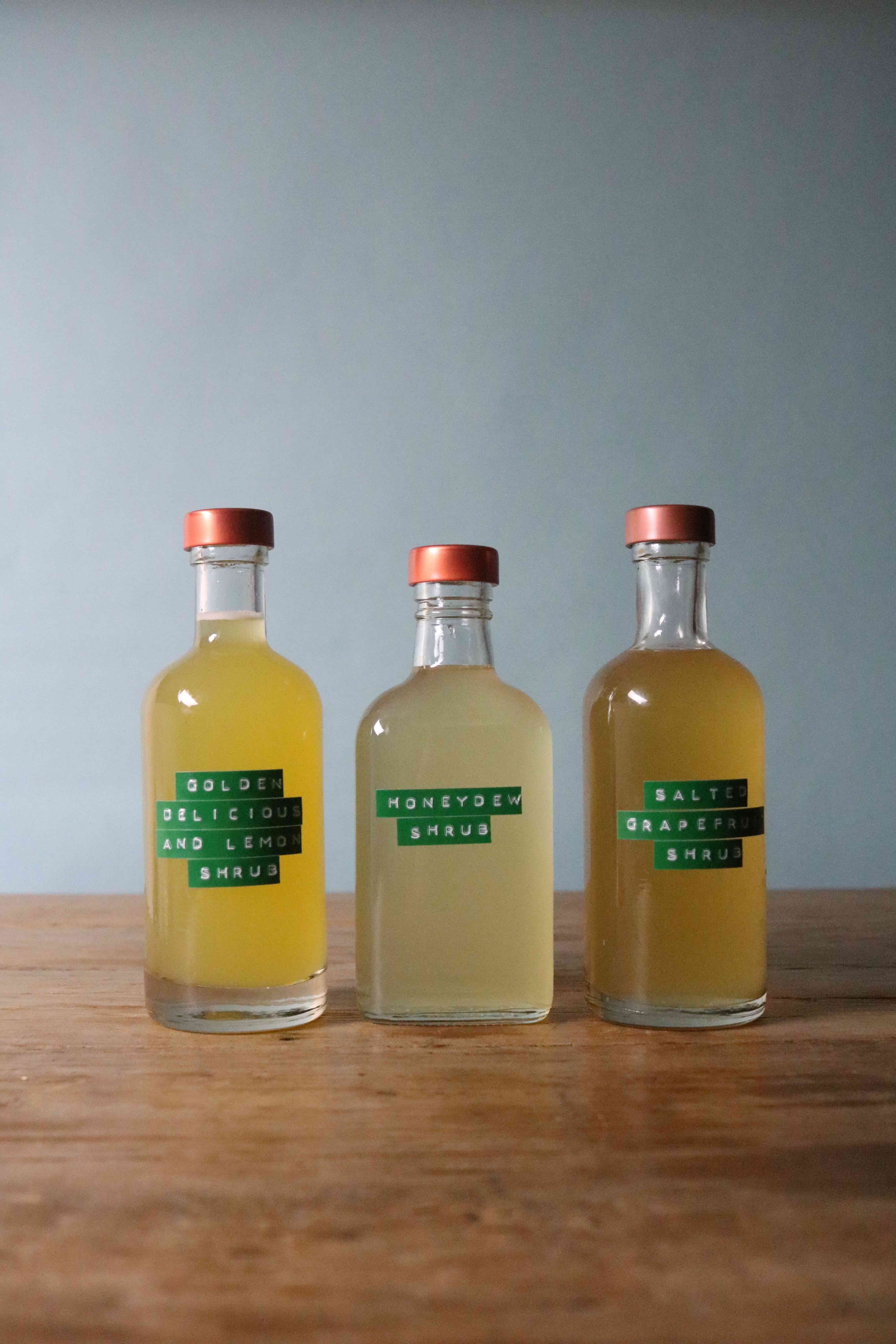 three bottles of distilled shrub materials such as honeydew, lemon shrub and grape