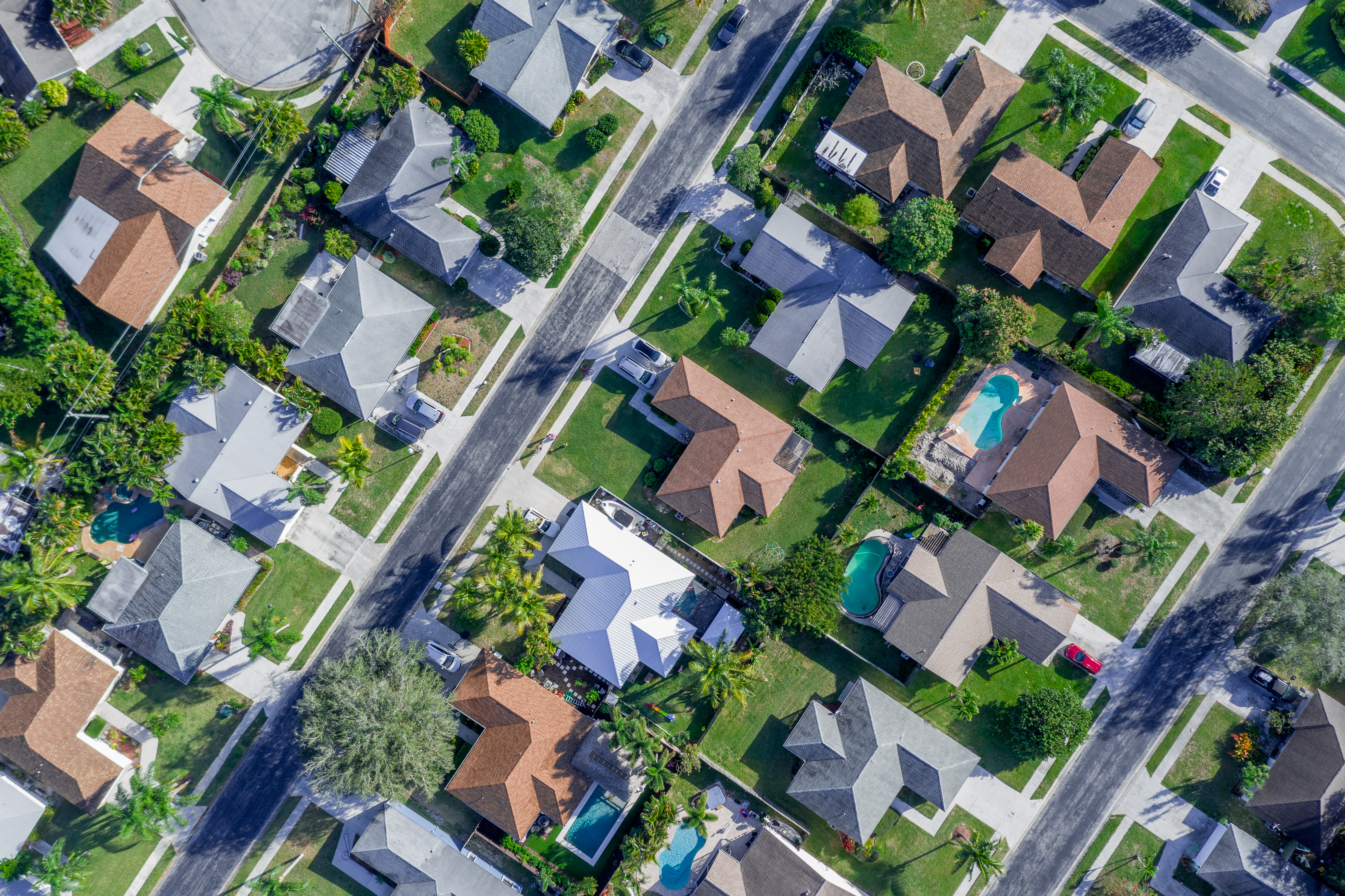 Bird's eye view of a suburb street with house roofs and bright green lawns  
