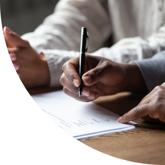 An image of two pairs of hands, one of which holds a pen above a contract, preparing to sign