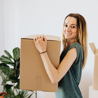 Dirty blonde woman holding a moving box in an apartment