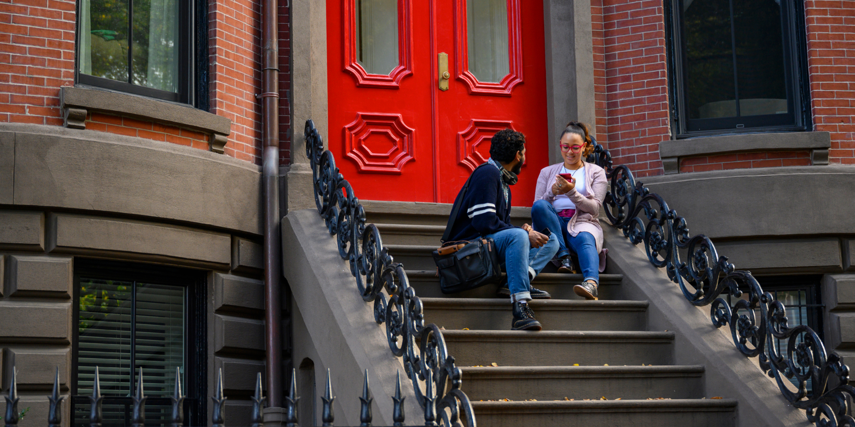 An image of two renters sitting on the stairs of a Brownstone with a bright red door 
