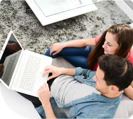 An image of a couple sitting and looking at a laptop and smiling