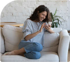 An image of a woman sitting on a couch and smiling at her phone