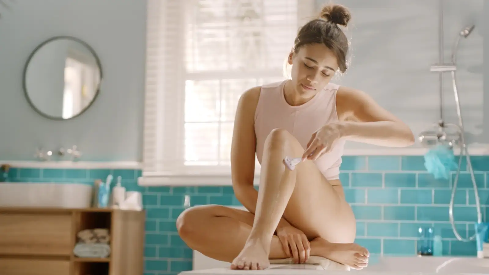 Mujer sentada en el suelo del baño y afeitándose las piernas con la maquinilla de afeitar Gillette Venus