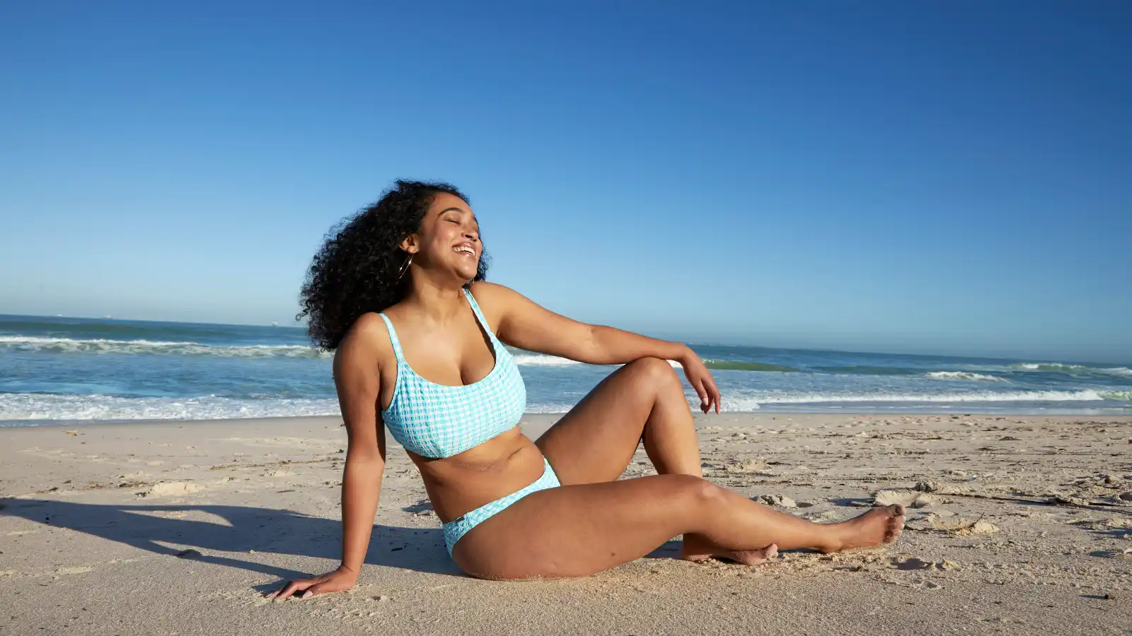 Mujer sentada en una playa de arena y sonriendo