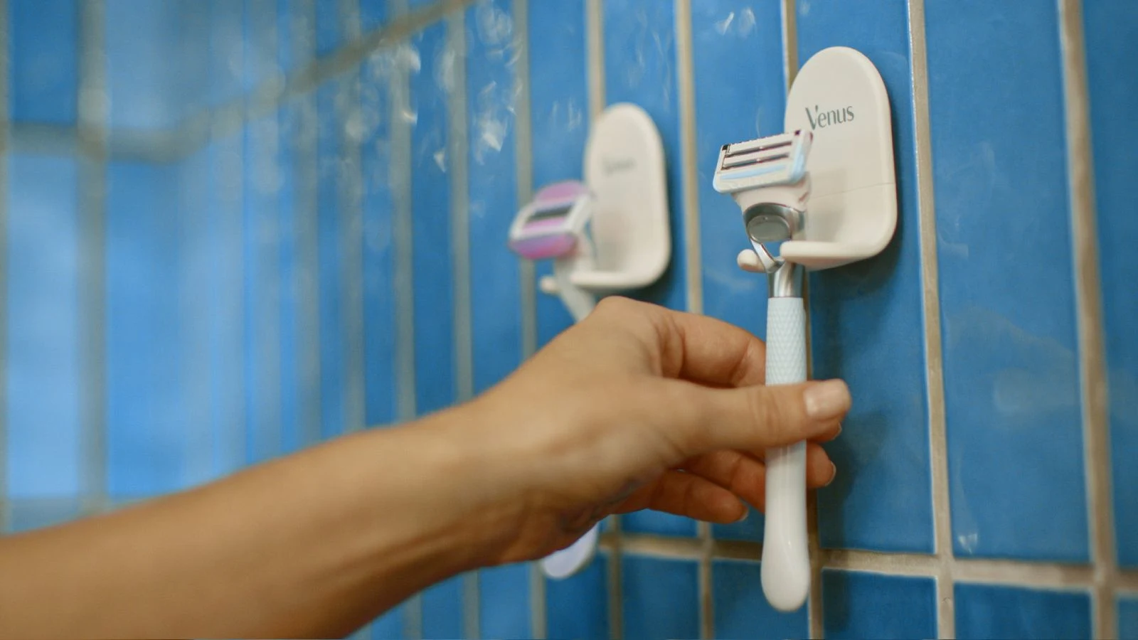 Mano de una mujer seleccionando una rasuradora Gillette Venus para depilarse la zona íntima dentro de la regadera o el baño