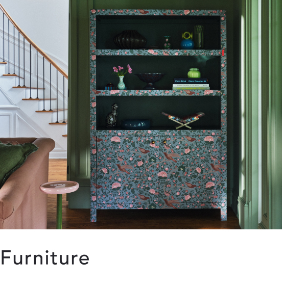 Floral-patterned bookshelf with dark shelves displaying decorative items, set against green wall trim near staircase.