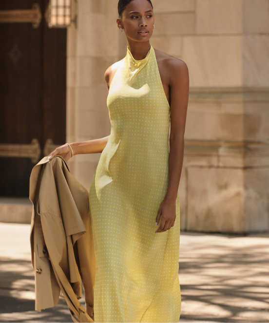 Woman in yellow halter maxi dress holding beige jacket with text "Dresses" overlaid on image